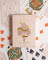 Premium-grade playing cards in pale pink with a gold-foiled tuck box featuring an ace of spades design with a snake wrapped around it. Perfect for games and gifting.