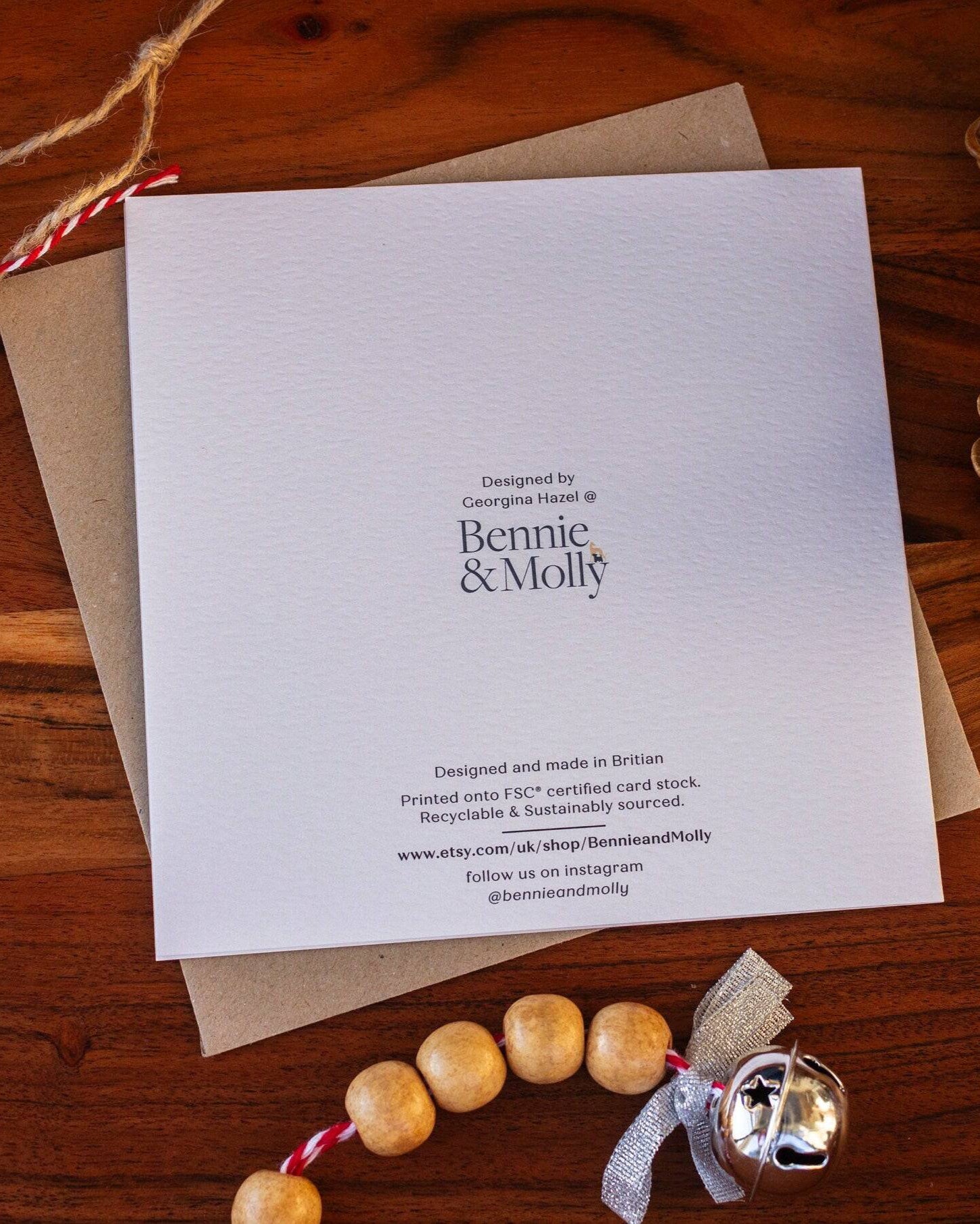 Handmade square Christmas card featuring a robin perched on a holly branch, printed on sustainably sourced textured paper with a biodegradable cello wrap and Kraft envelope.