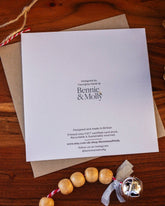 Handmade square Christmas card featuring a robin perched on a holly branch, printed on sustainably sourced textured paper with a biodegradable cello wrap and Kraft envelope.