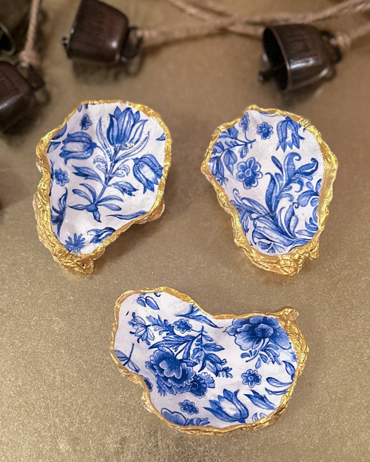 Set of three handmade oyster shell trinket dishes with blue and white floral designs, featuring a decoupage technique and hand-painted gold edges, ideal for home decor or jewellery storage.