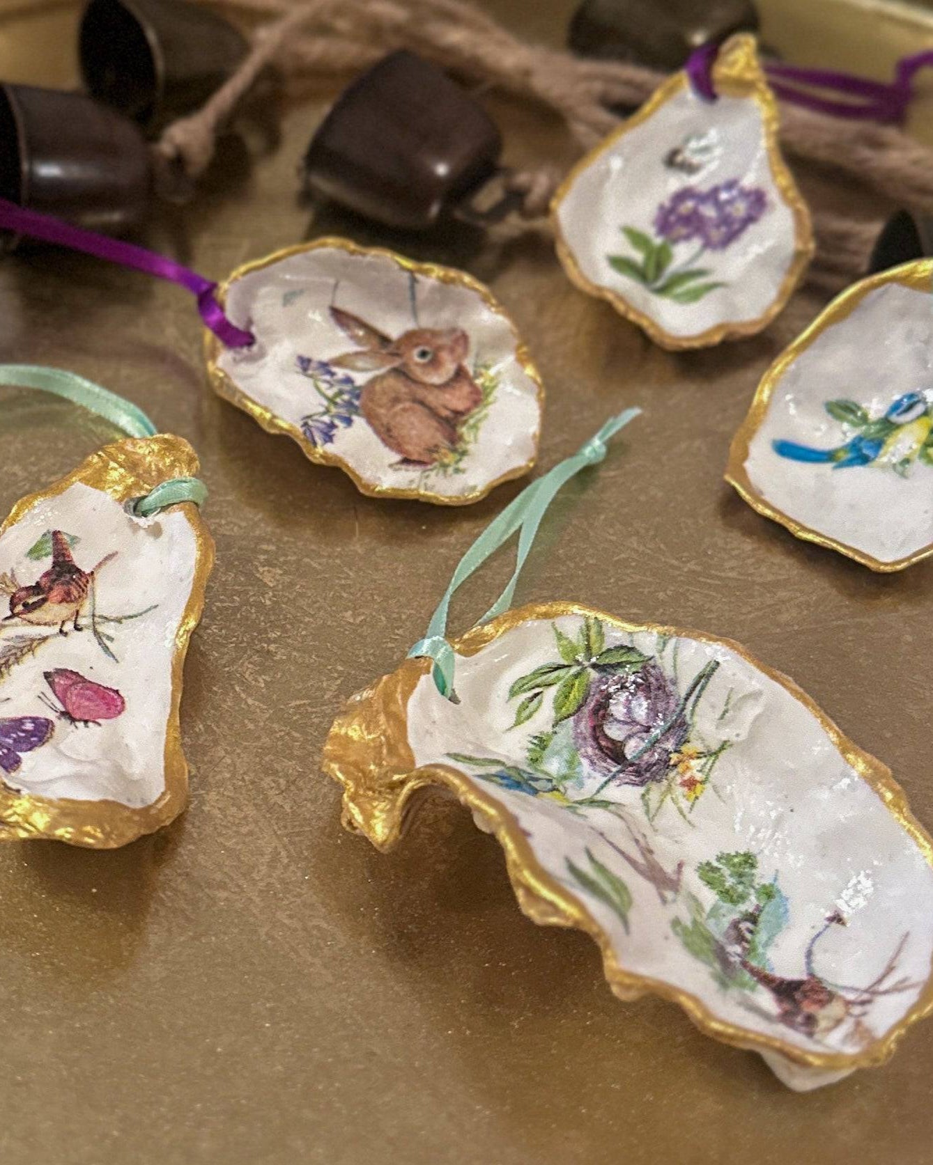 Set of five handmade Easter hanging ornaments crafted from oyster shells, featuring a decoupage technique with hand-painted gold edges, decorated with spring motifs like bunnies, flowers, and bees, perfect for Easter or spring decor.