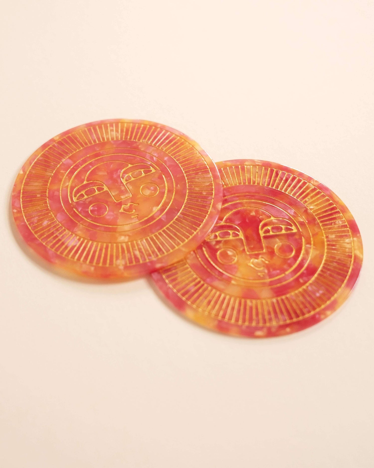 Set of two round handmade coasters in passionfruit pink acetate with engraved, gold-filled Sol face detail. Suitable for indoor or outdoor use. Perfect for home décor or barware.