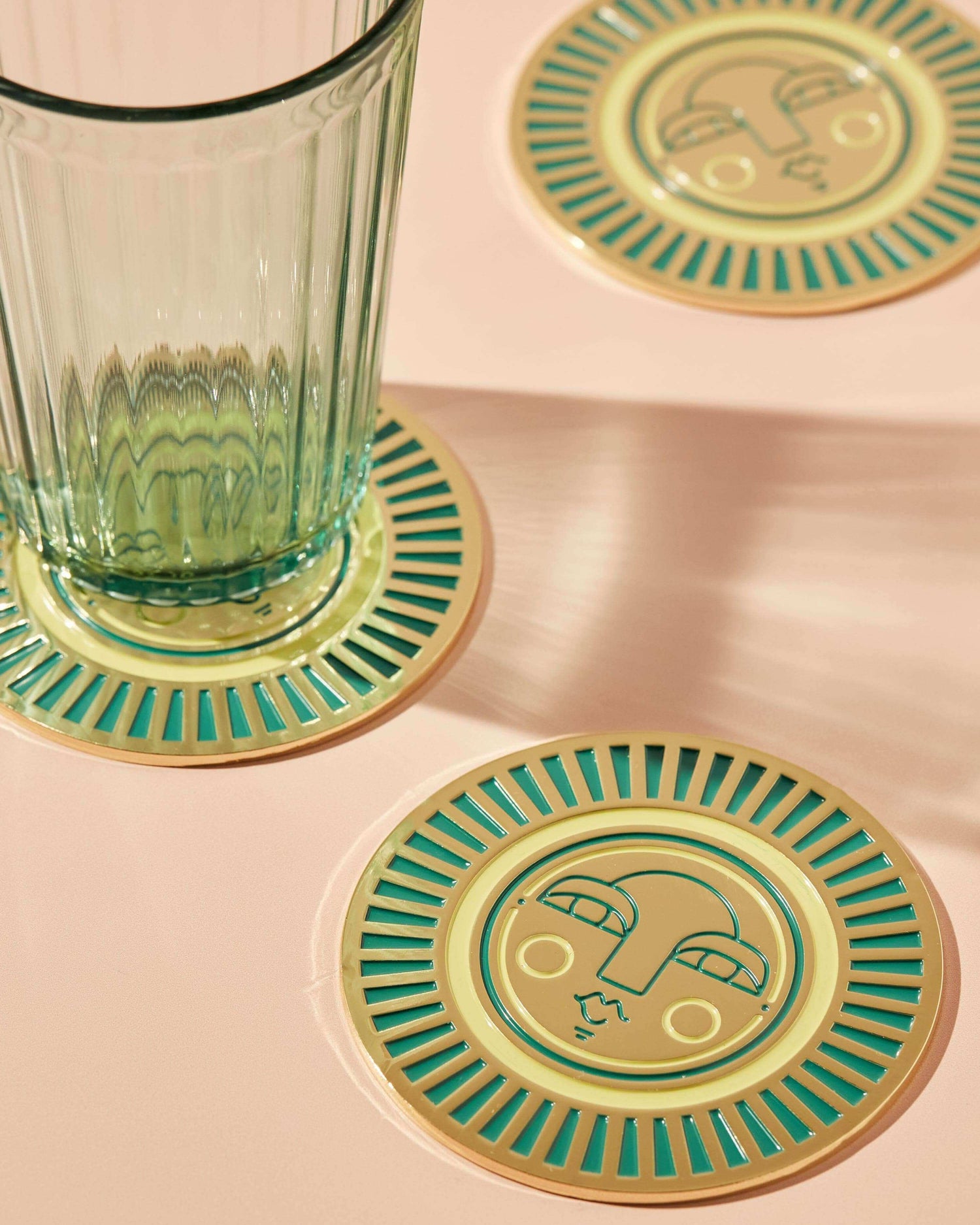 Round handmade teal coasters with gold-coloured metal and enamel, featuring the Sol face design. Perfect for home decor or barware.