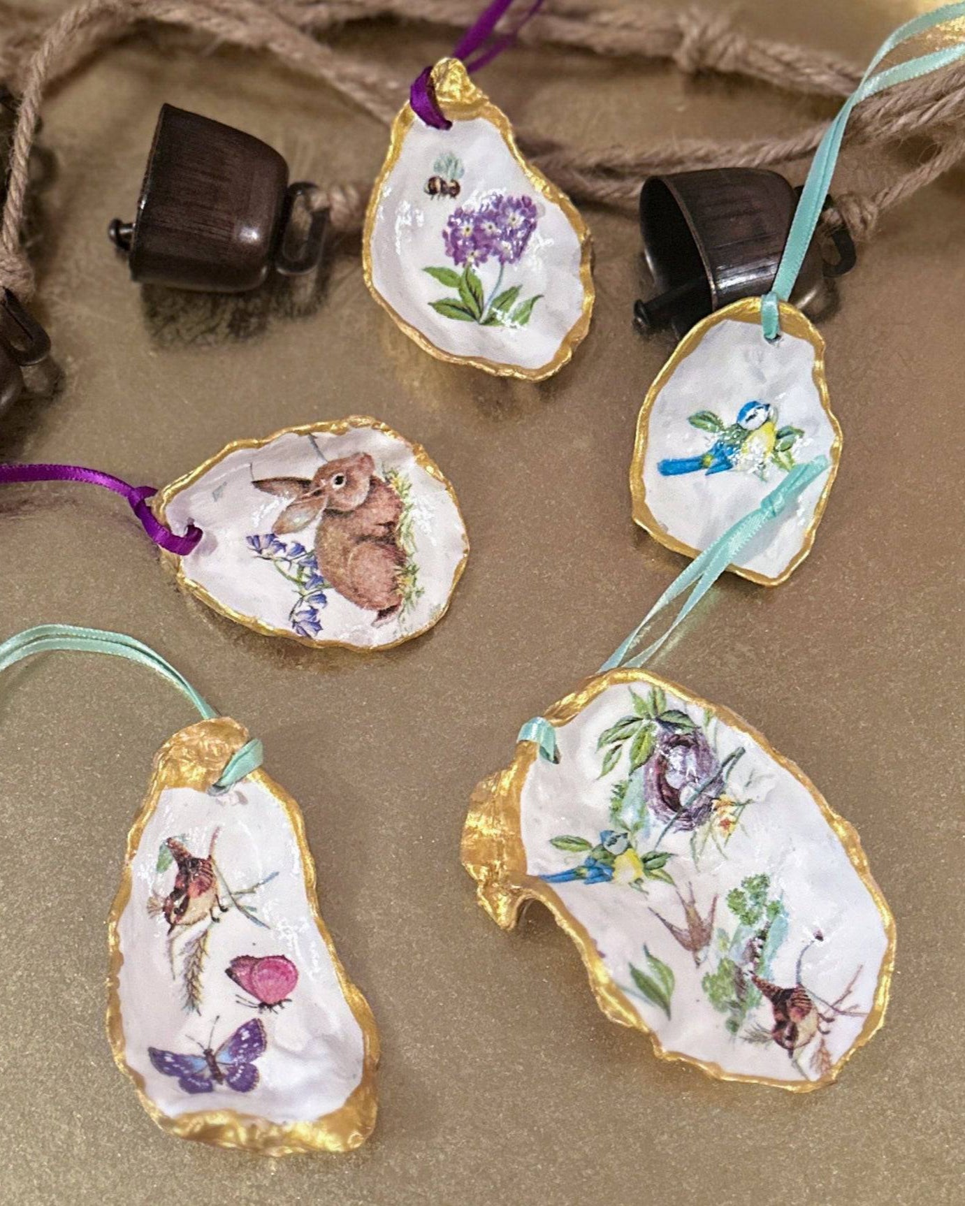 Set of five handmade Easter hanging ornaments crafted from oyster shells, featuring a decoupage technique with hand-painted gold edges, decorated with spring motifs like bunnies, flowers, and bees, perfect for Easter or spring decor.