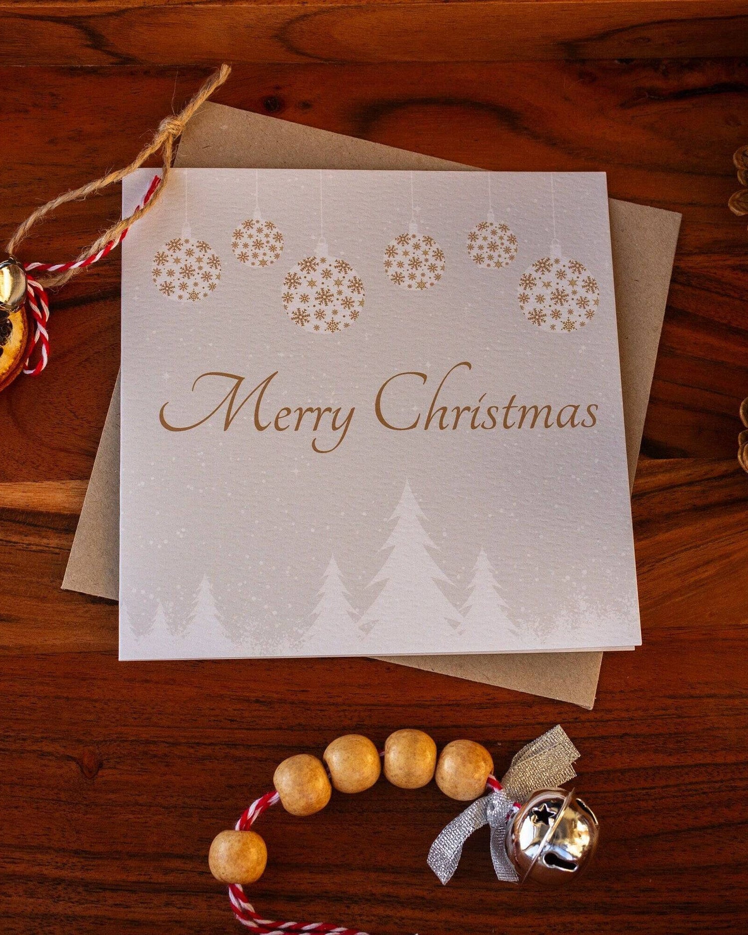 Square Christmas card with white snowy trees, hanging gold and white baubles, and "Merry Christmas" written in gold. Made from recyclable luxury textured paper with eco-friendly packaging.