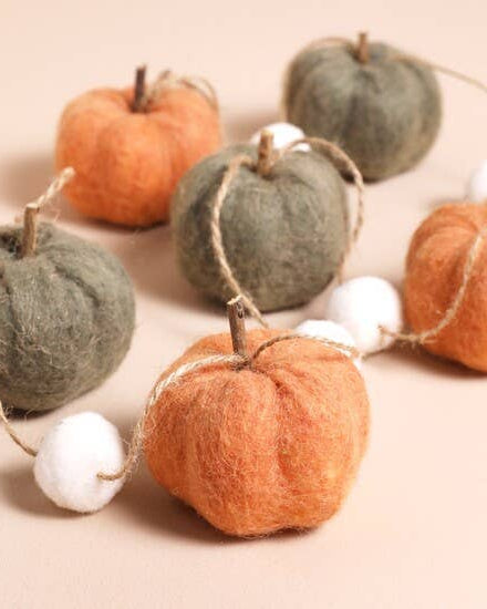 Decorative string of felt pumpkins and apples on a beige background