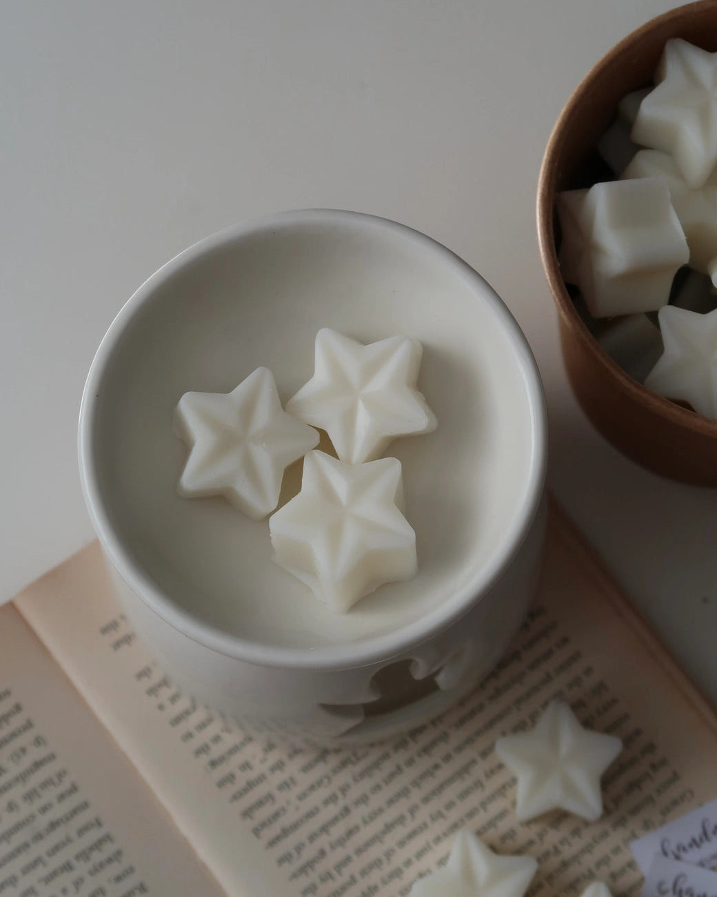 Star-shaped white candies in a white bowl on a light surface with a book underneath.