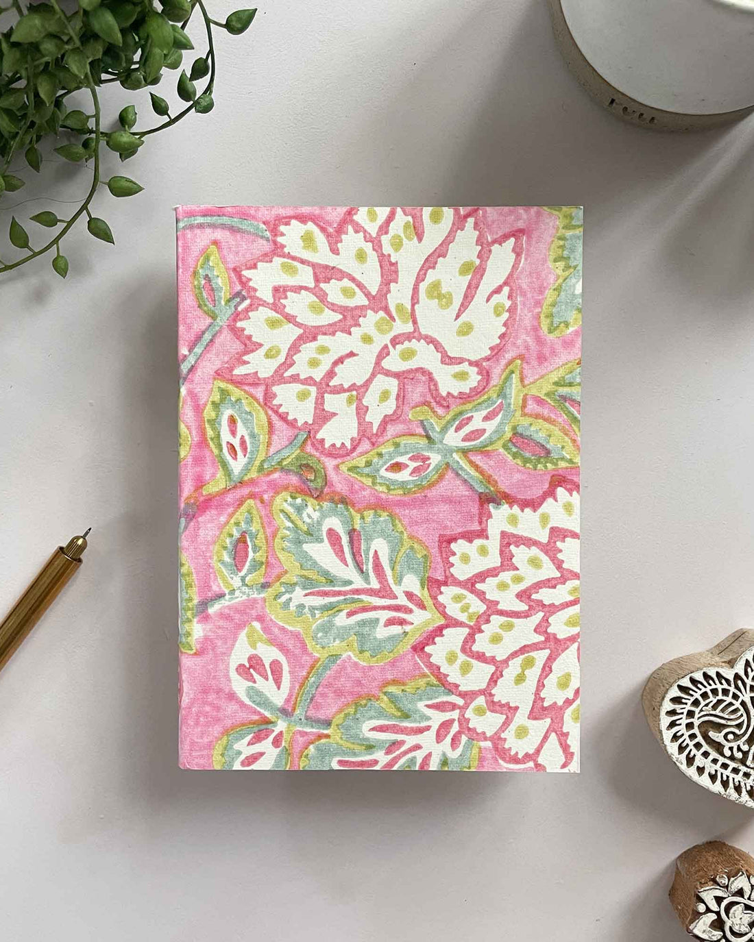 Notebook with pink floral pattern on a white surface with decorative items.