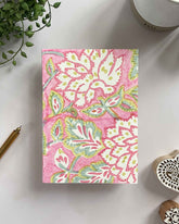 Notebook with pink floral pattern on a white surface with decorative items.