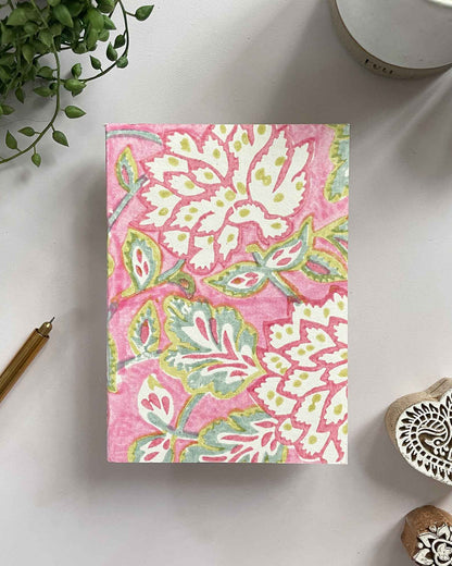 Notebook with pink floral pattern on a white surface with decorative items.