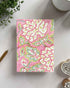 Notebook with pink floral pattern on a white surface with decorative items.