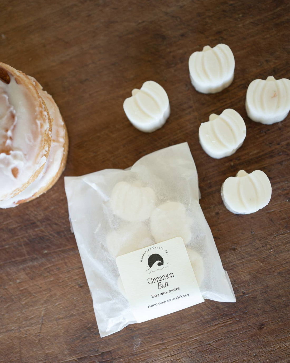 White wax melts in pumpkin shapes on a wooden surface with a branded paper bag.