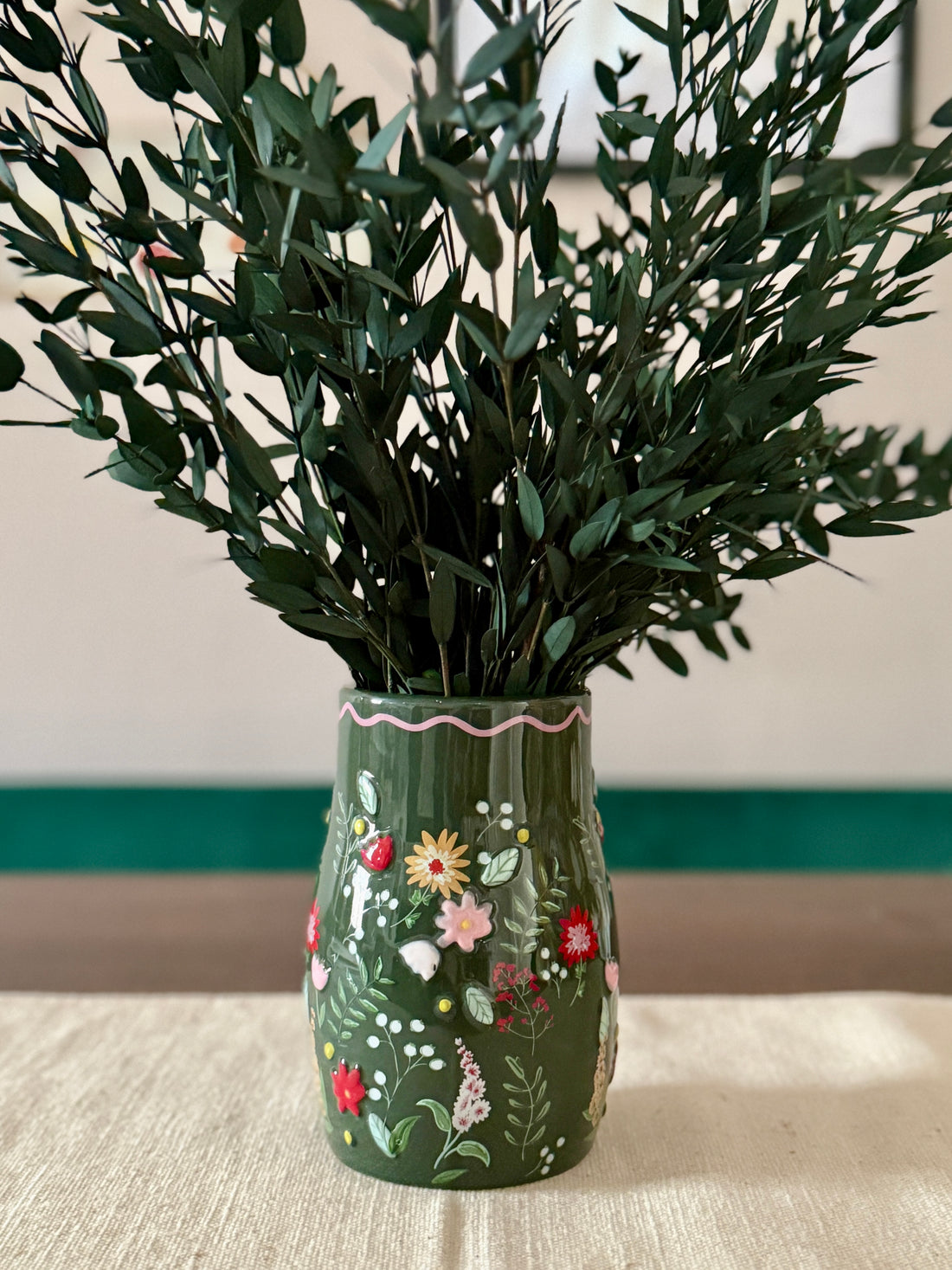 Decorative vase with floral patterns containing green plants on a neutral background