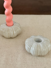 Decorative candle holders with a pink textured candle on a beige surface