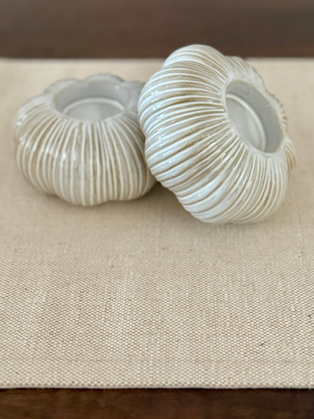 Two white textured candle holders on a beige surface