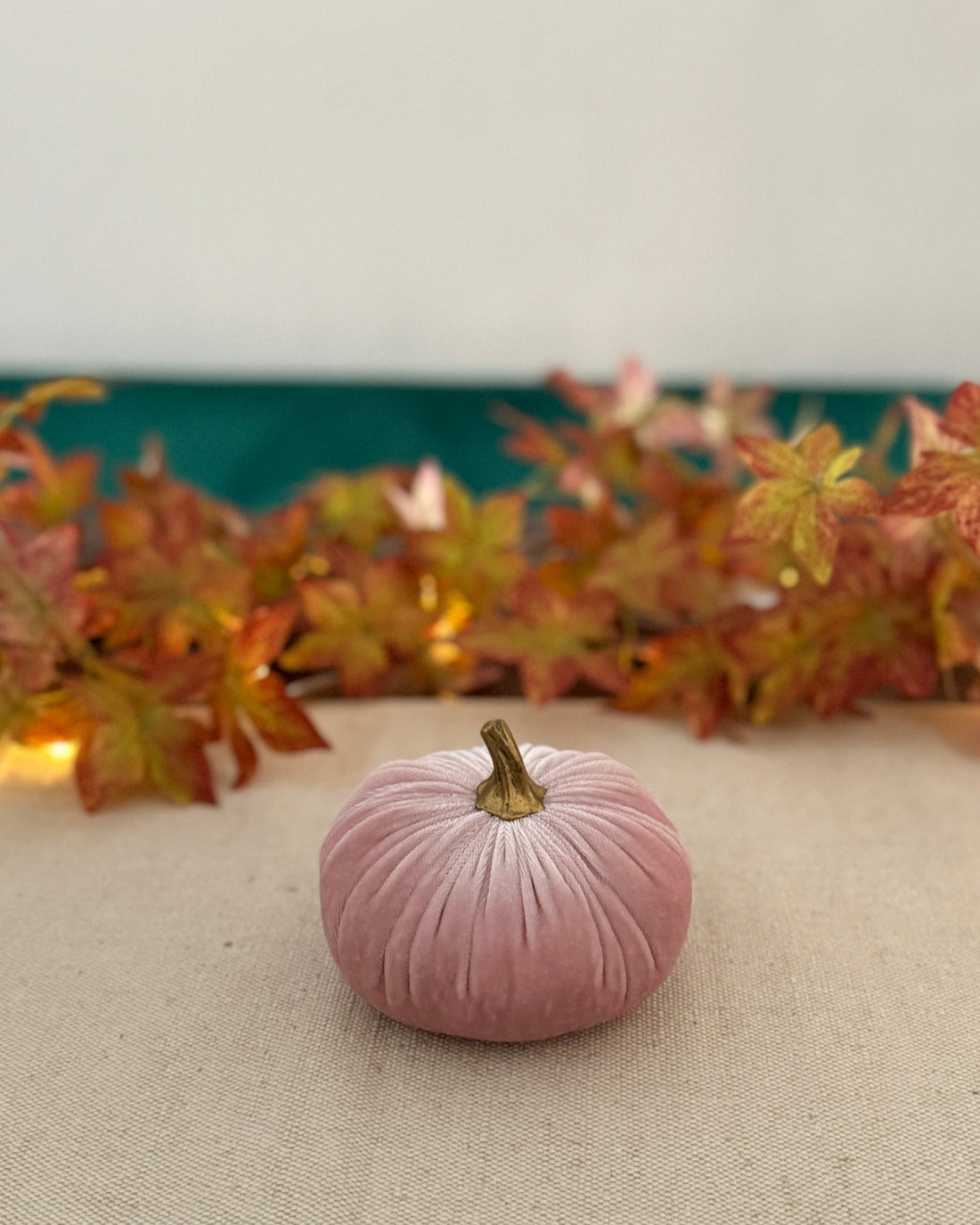 Pink velvet pumpkin on a beige surface with autumn leaves in the background