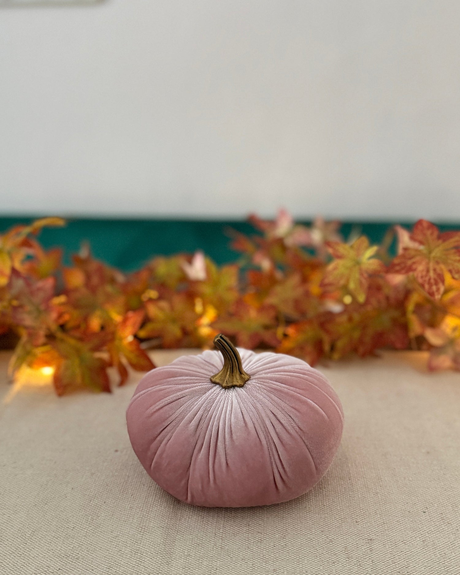 Pink velvet pumpkin on a neutral surface with autumn leaves in the background