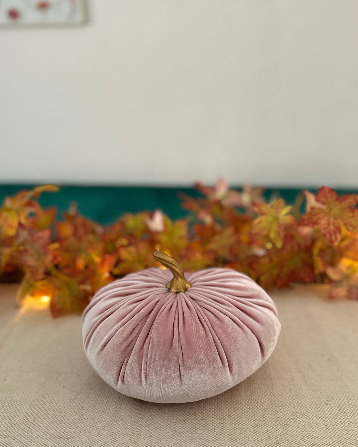Pink velvet pumpkin on a table with autumn leaves in the background
