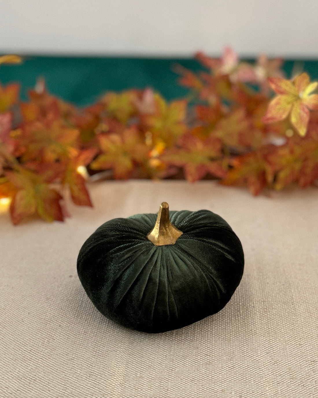 Small green pumpkin on a beige surface with autumn leaves in the background