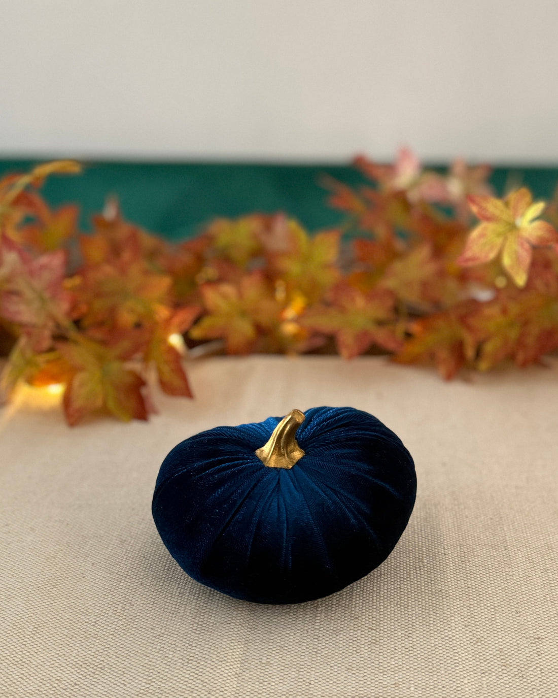 Blue velvet pumpkin on a beige surface with autumn leaves in the background