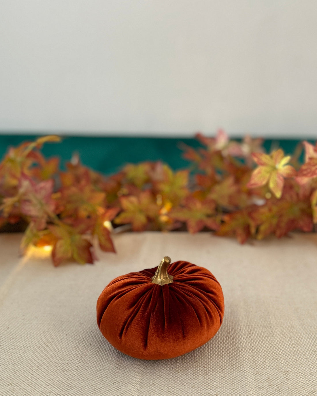 Small orange velvet pumpkin on a beige surface with autumn leaves in the background.