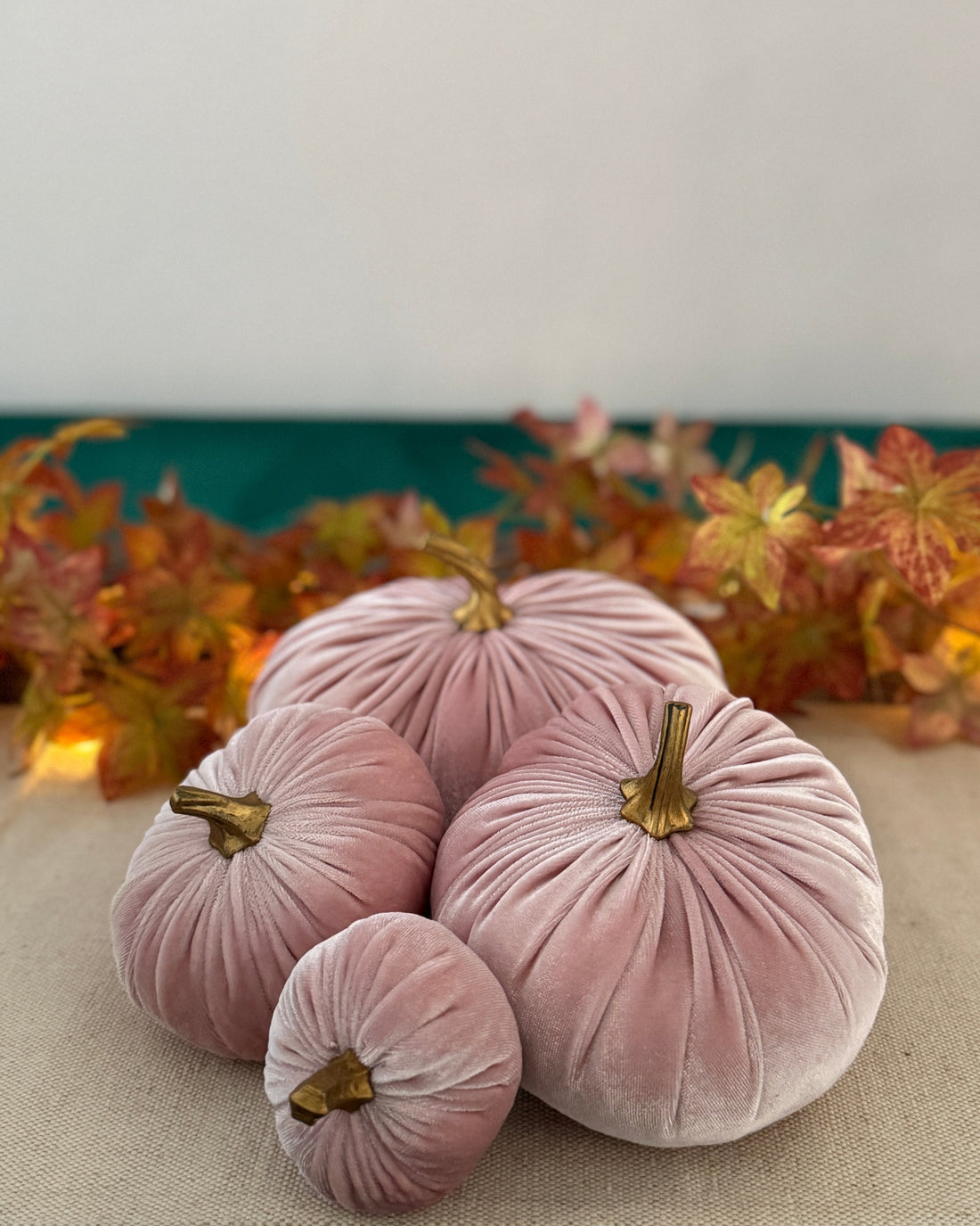 Pink velvet pumpkins on a table with autumn leaves in the background