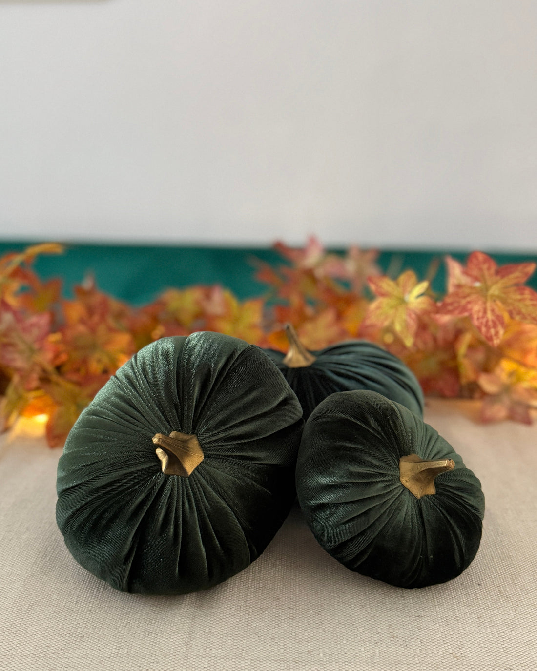 Two green velvet pumpkins on a table with a decorative background