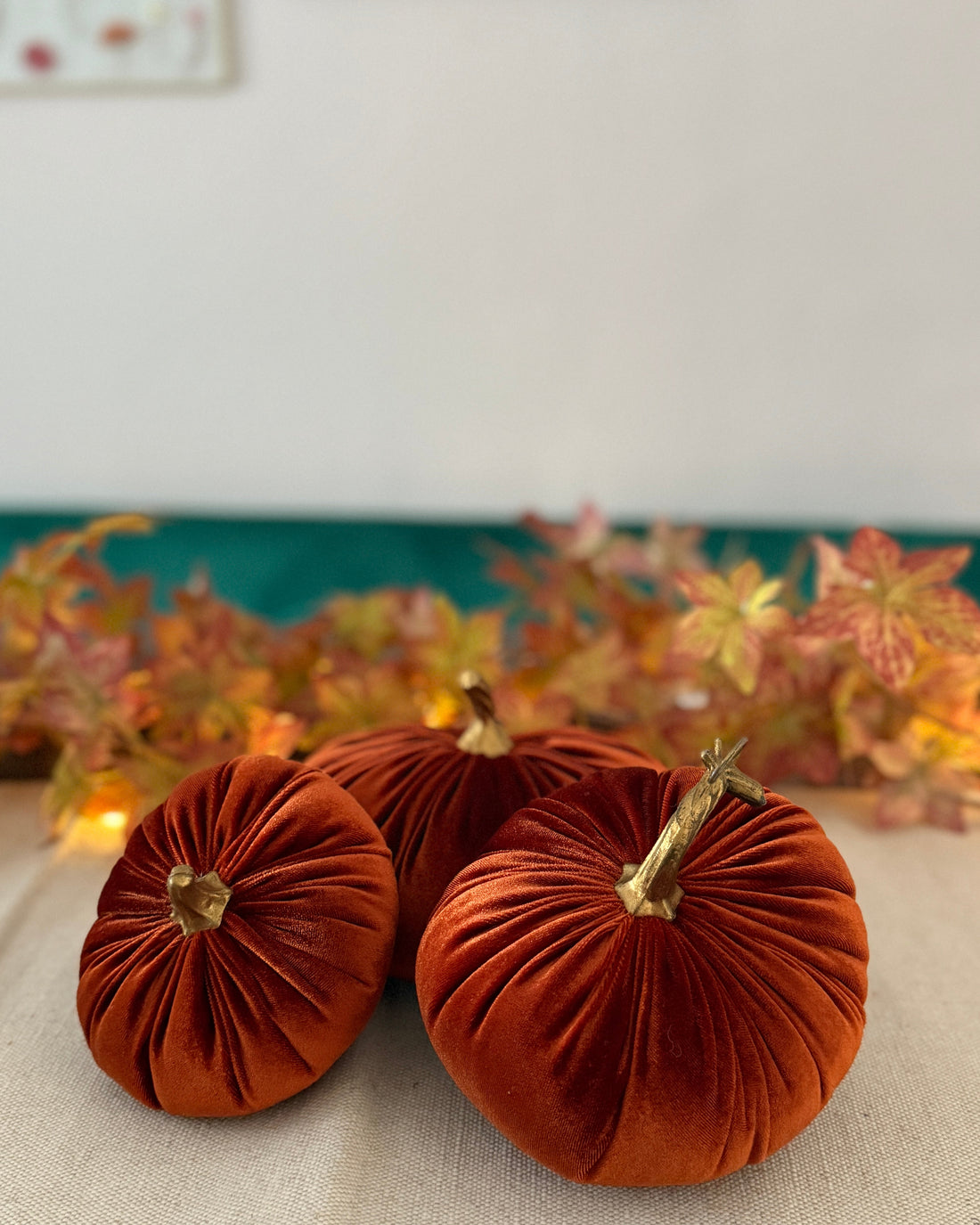 Three orange velvet pumpkins on a table with a decorative background
