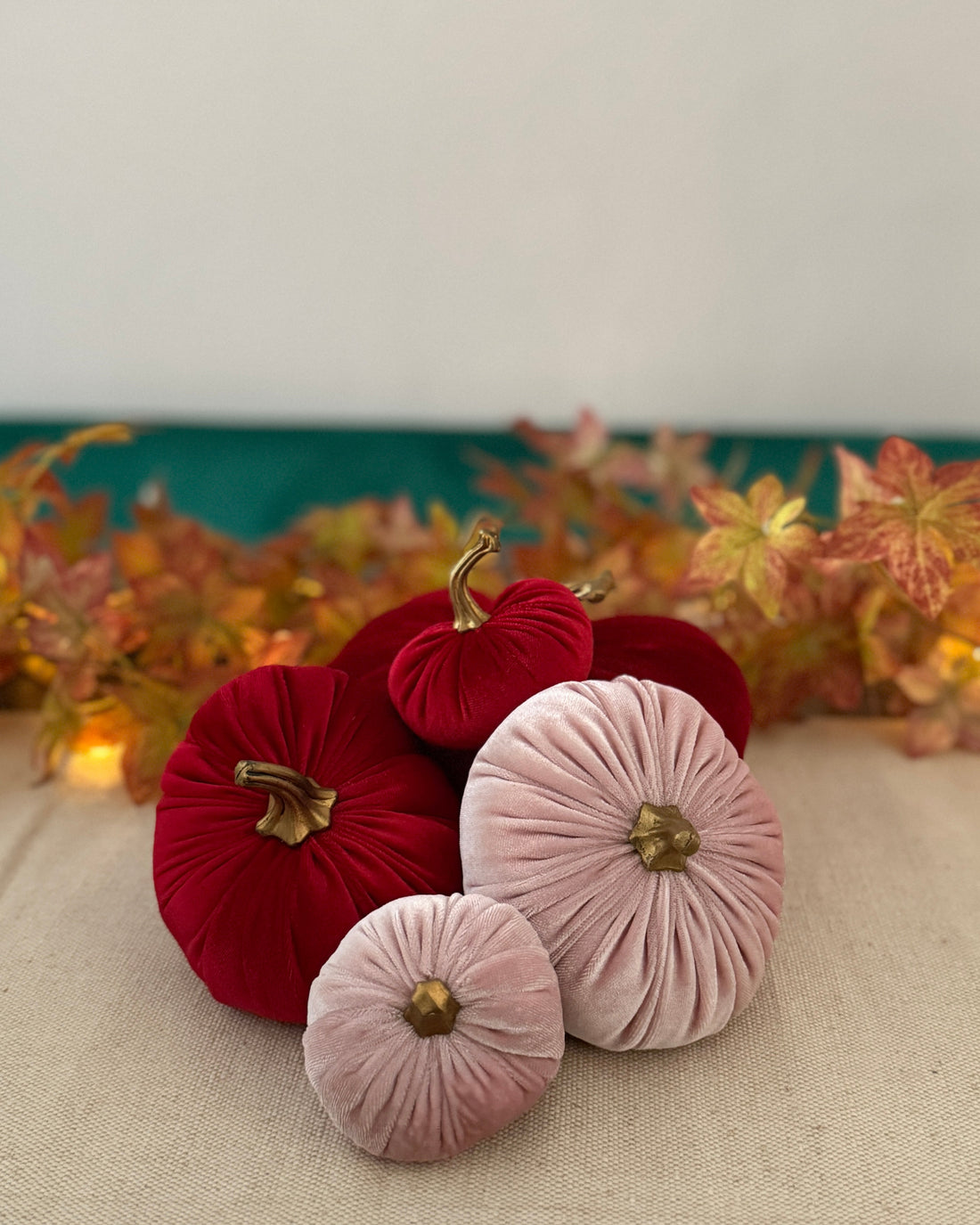 Decorative pumpkins made of red and pink fabric with gold accents on a neutral surface.
