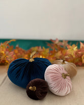 Decorative pumpkins in navy, pink, and brown on a table with a floral arrangement in the background.