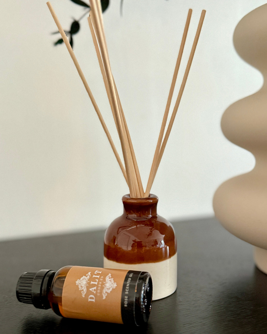 Diffuser bottle with reeds and a small bottle of essential oil on a dark surface.