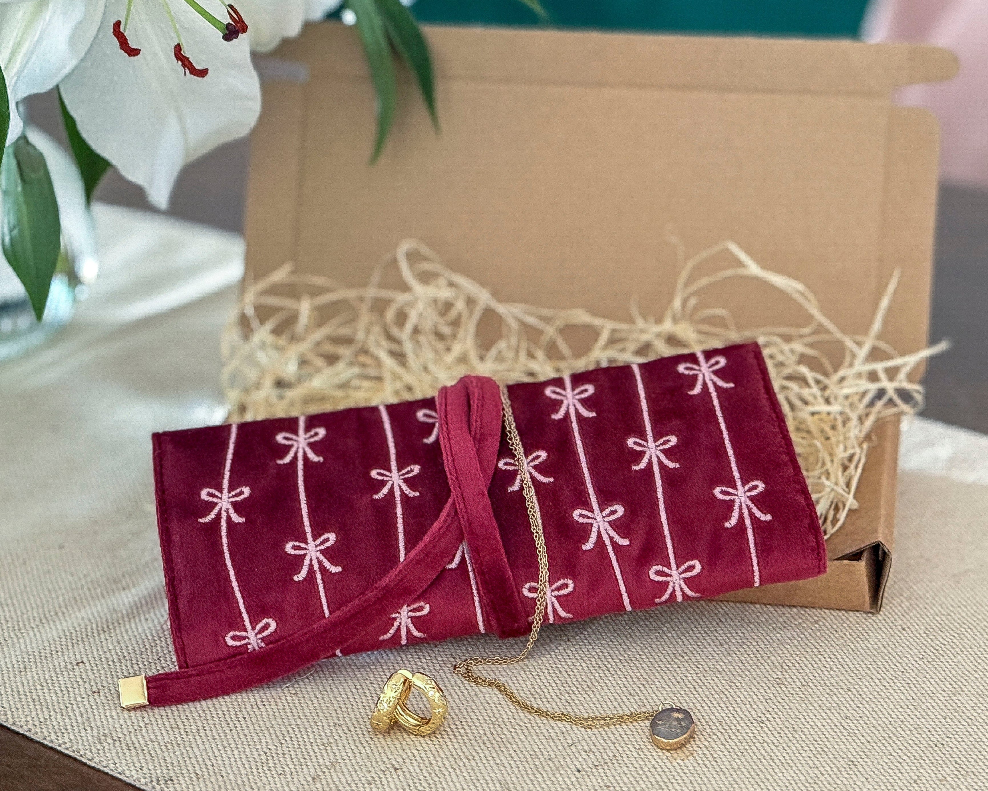 Red jewelry pouch with white patterns on a beige surface, with a gold ring and necklace displayed.