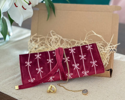 Red jewelry pouch with white patterns on a beige surface, with a gold ring and necklace displayed.