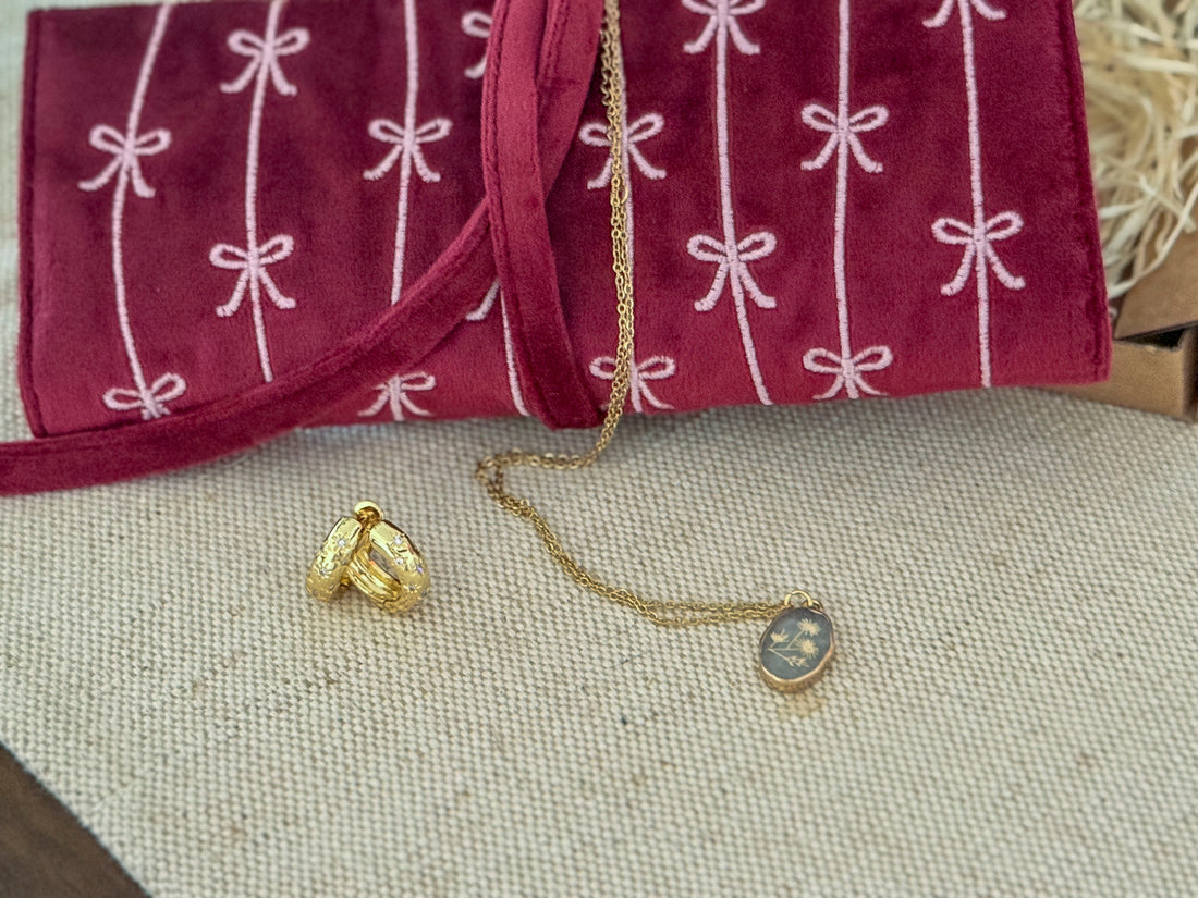 Gold necklace and earrings on a textured surface with a purple fabric with white patterns in the background.