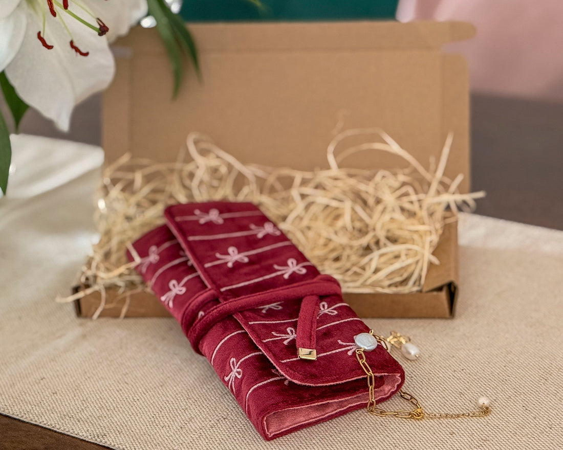 Red jewelry case with gold jewelry on a beige surface with flowers in the background