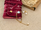 Jewelry set with pearls and gold chain on a textured surface, next to a folded red fabric with white patterns.