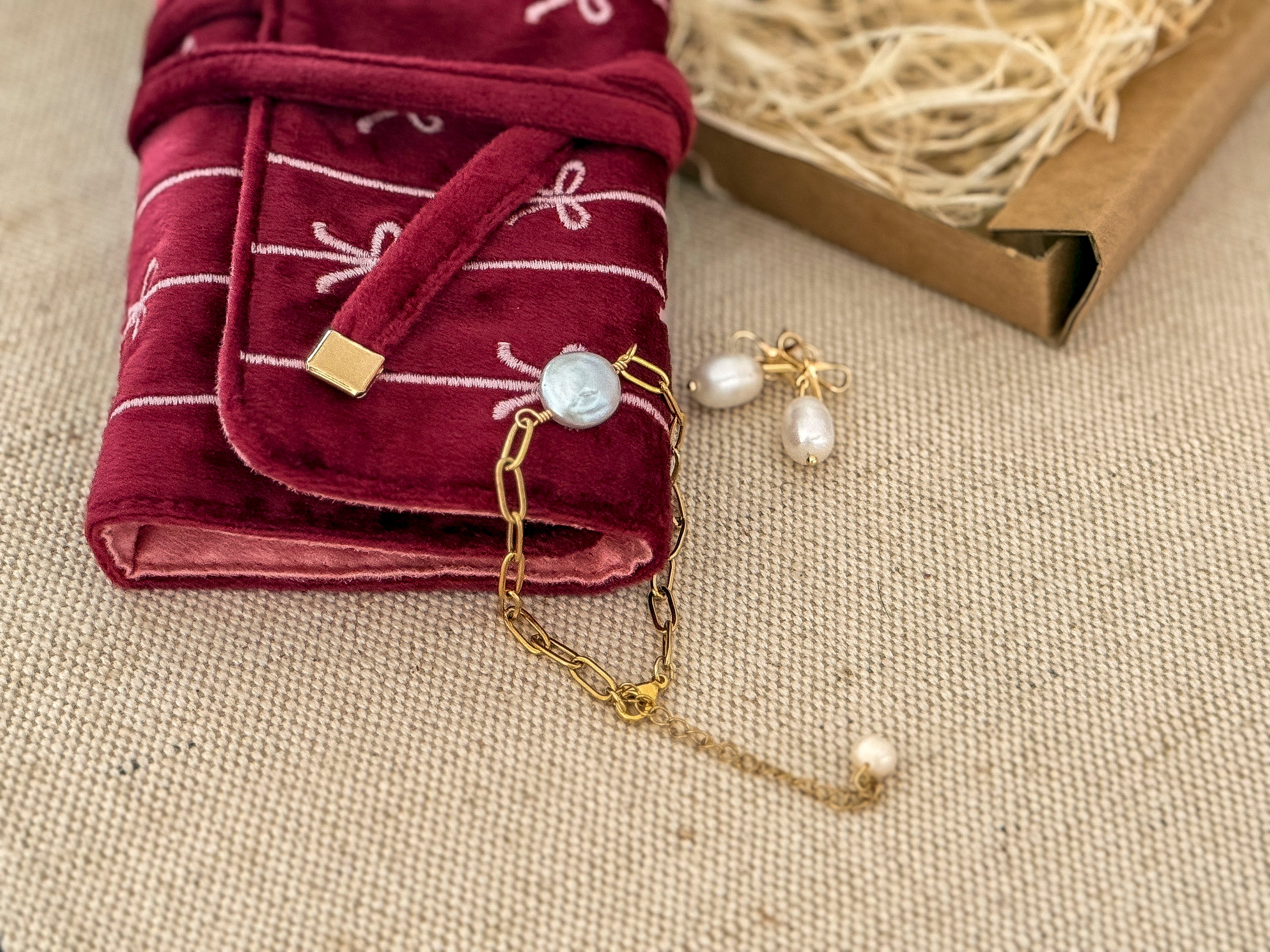Jewelry set with pearls and gold chain on a textured surface, next to a folded red fabric with white patterns.