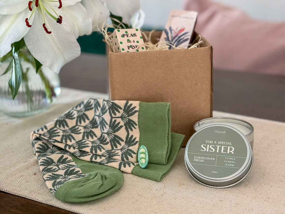 Gift set with socks, a candle, and a card on a table with flowers in the background.