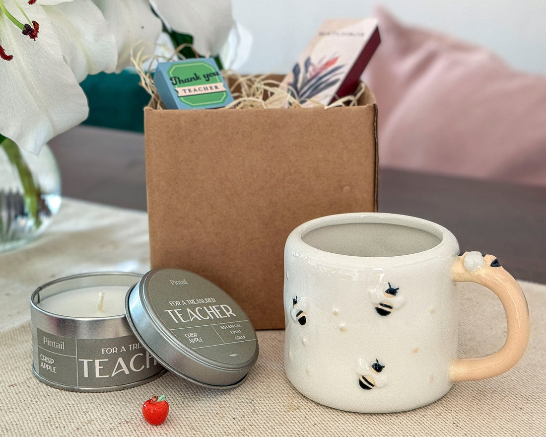 Ceramic mug with decorative elements, candle, and gift box on a table.