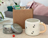 Ceramic mug with decorative elements, candle, and gift box on a table.