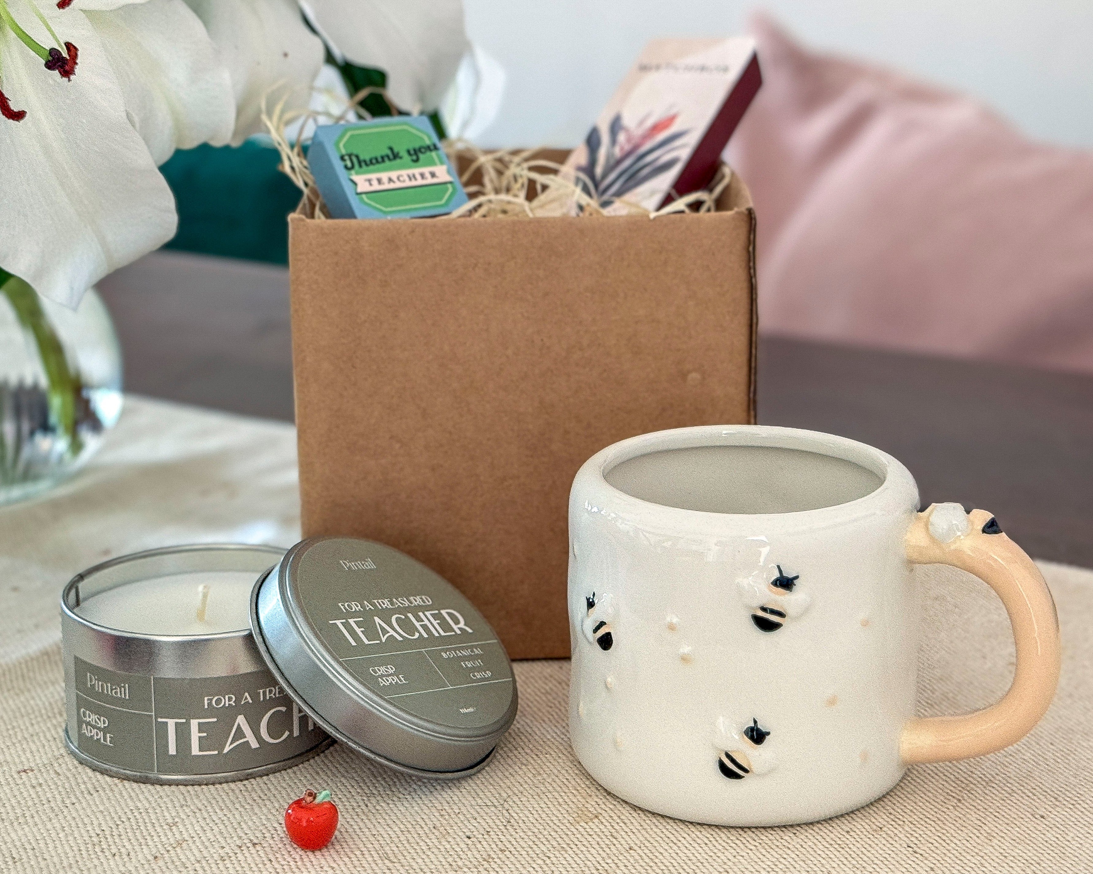 Ceramic mug with decorative elements, candle, and gift box on a table.