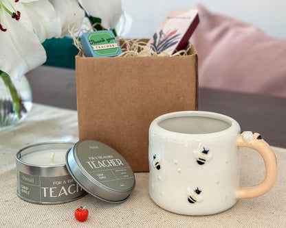 Ceramic mug with decorative elements, candle, and gift box on a table.