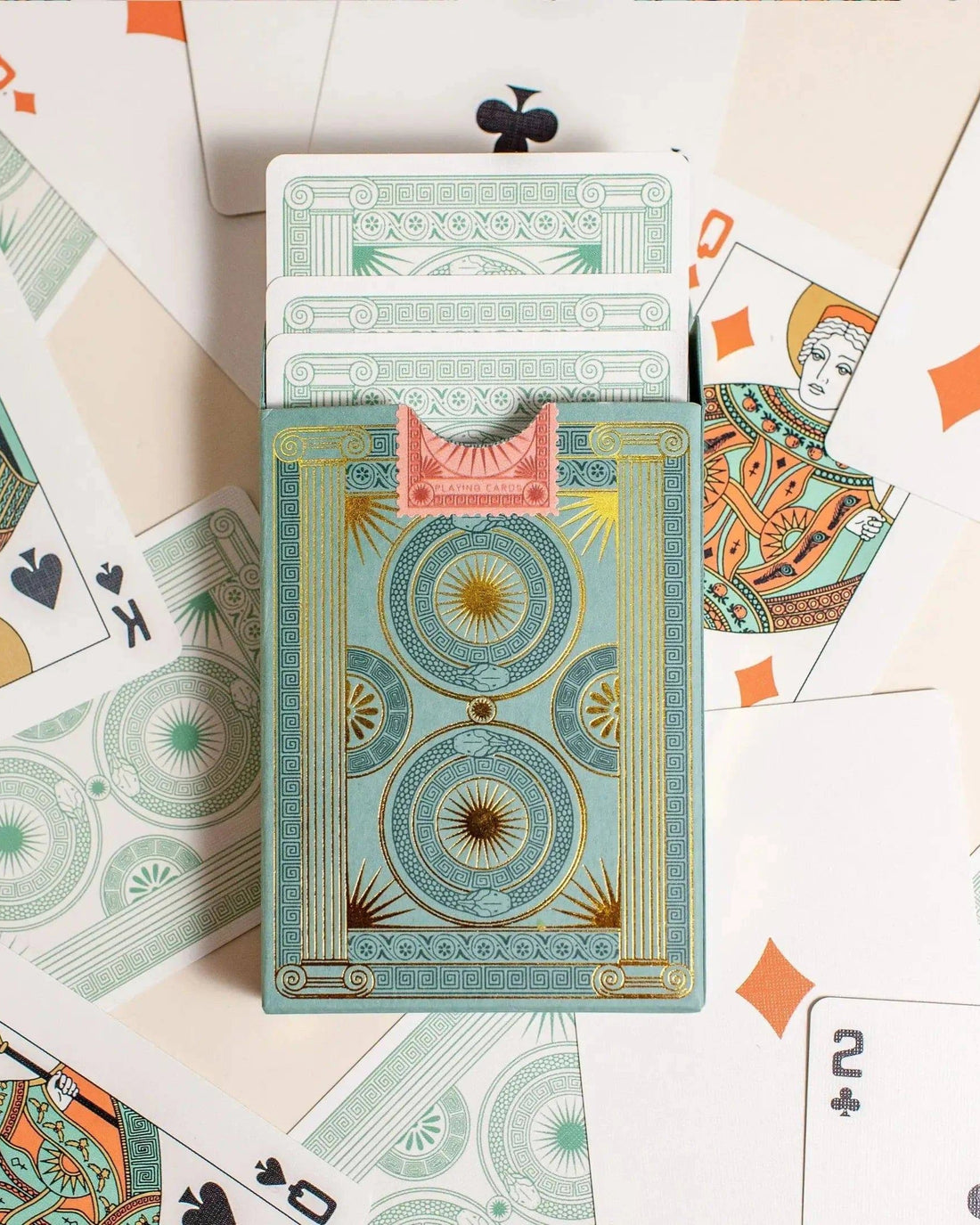 Premium-grade playing cards in sage green with a gold-foiled tuck box featuring an ace of spades design with a snake wrapped around it. Back of box with cards coming out surrounded by cards