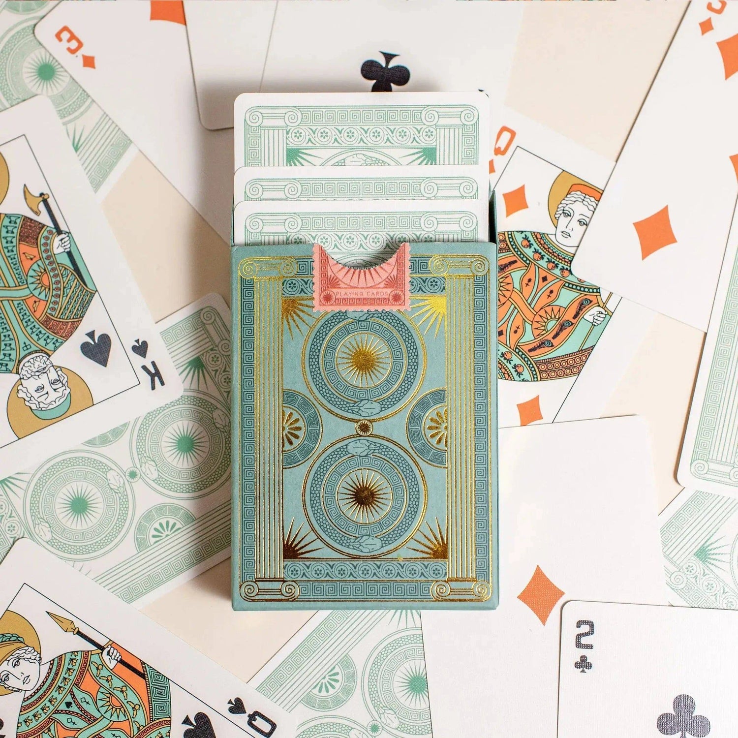 Premium-grade playing cards in sage green with a gold-foiled tuck box featuring an ace of spades design with a snake wrapped around it. Back of box with cards coming out surrounded by cards