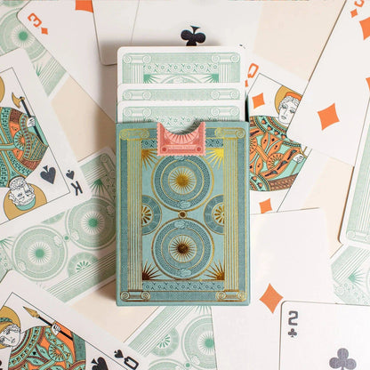Premium-grade playing cards in sage green with a gold-foiled tuck box featuring an ace of spades design with a snake wrapped around it. Back of box with cards coming out surrounded by cards