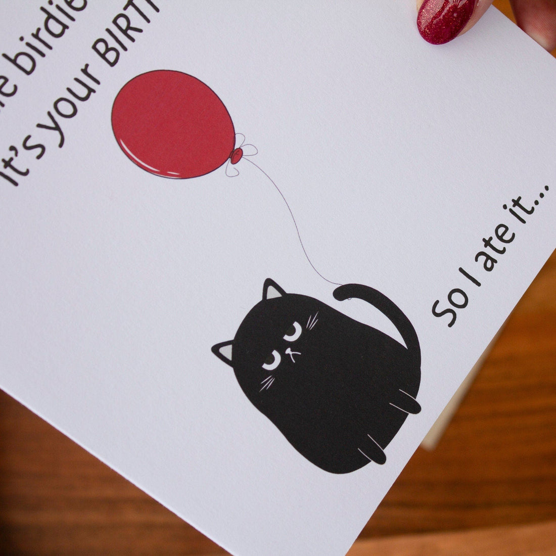 Square birthday card with a humorous black cat illustration holding a red balloon and text: &quot;A little birdie told me it’s your birthday, so I ate it.&quot; Made with sustainable materials.