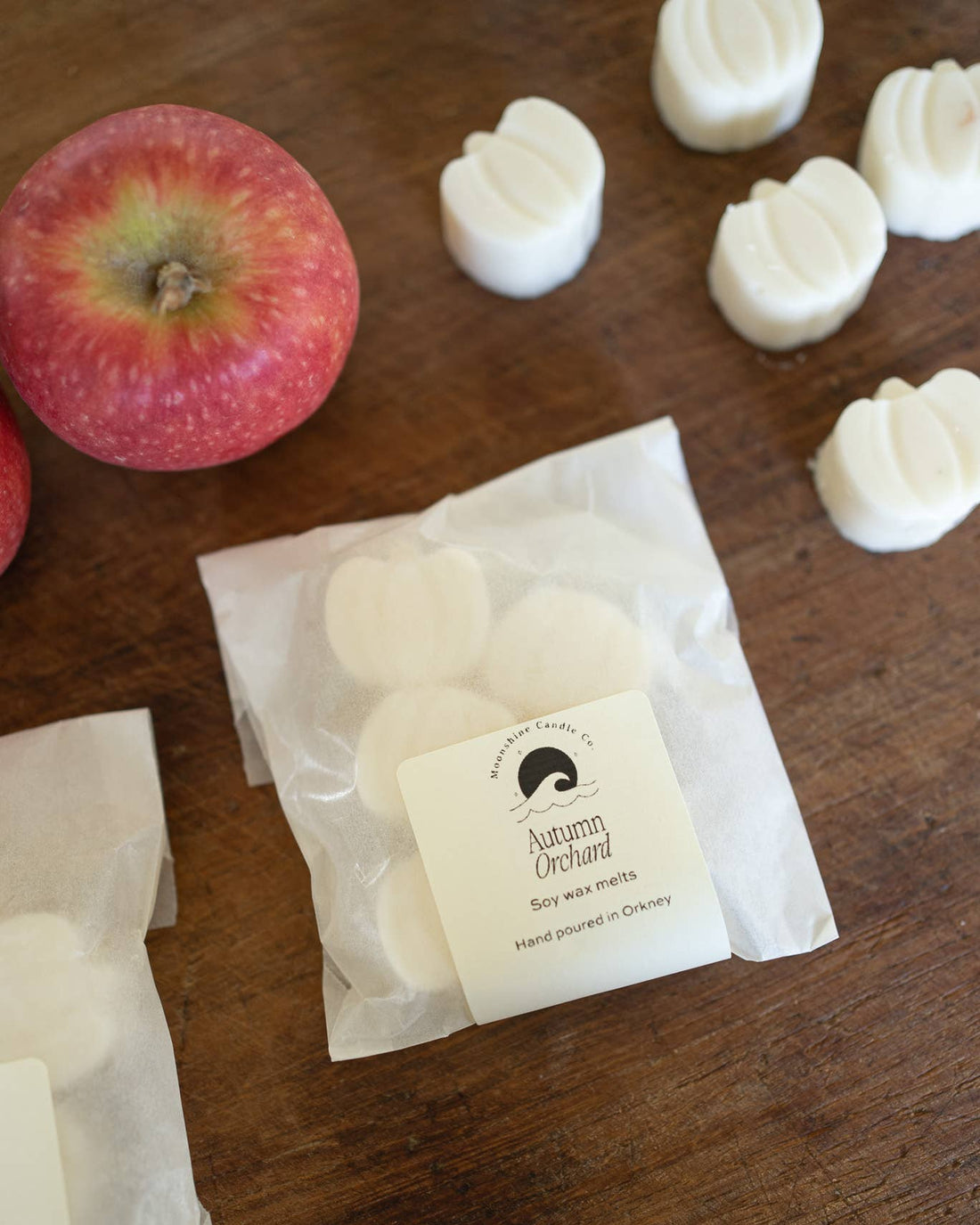 White soy wax melts in a clear bag with a label on a wooden surface, next to an apple.