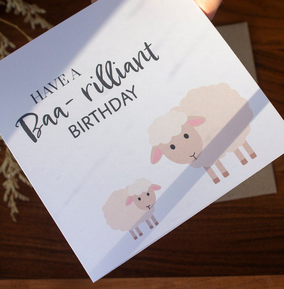 Square handmade birthday card with a sheep and lamb illustration and &quot;Have a Baa-rilliant Birthday&quot; text. Made in the UK using sustainable card stock and eco-friendly packaging.