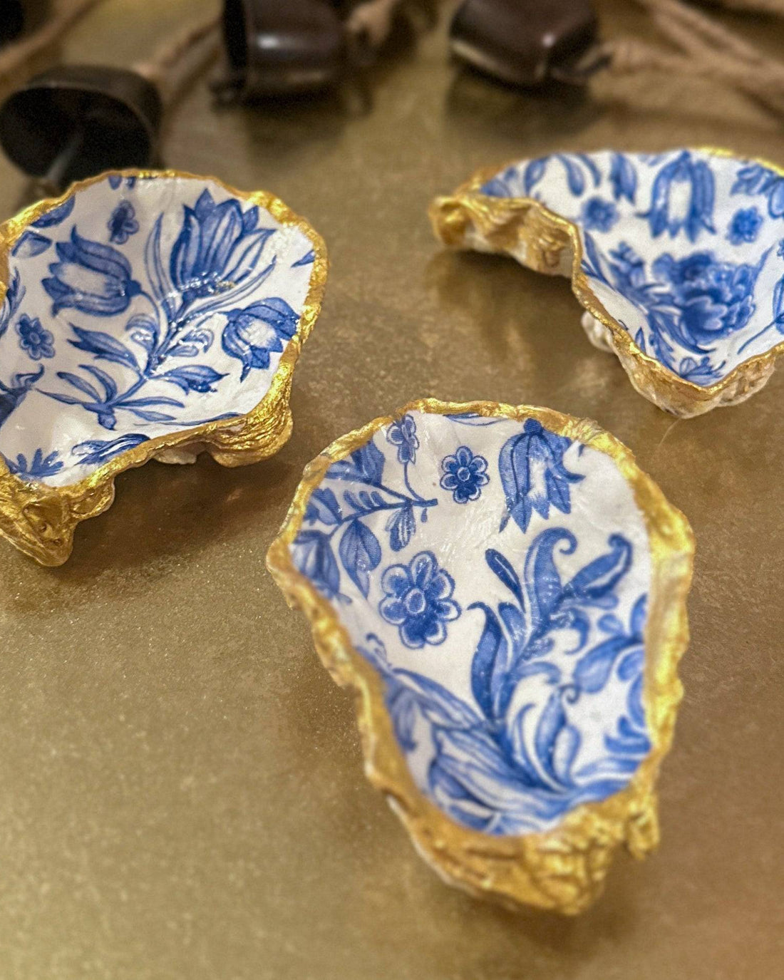Set of three handmade oyster shell trinket dishes with blue and white floral designs, featuring a decoupage technique and hand-painted gold edges, ideal for home decor or jewellery storage.