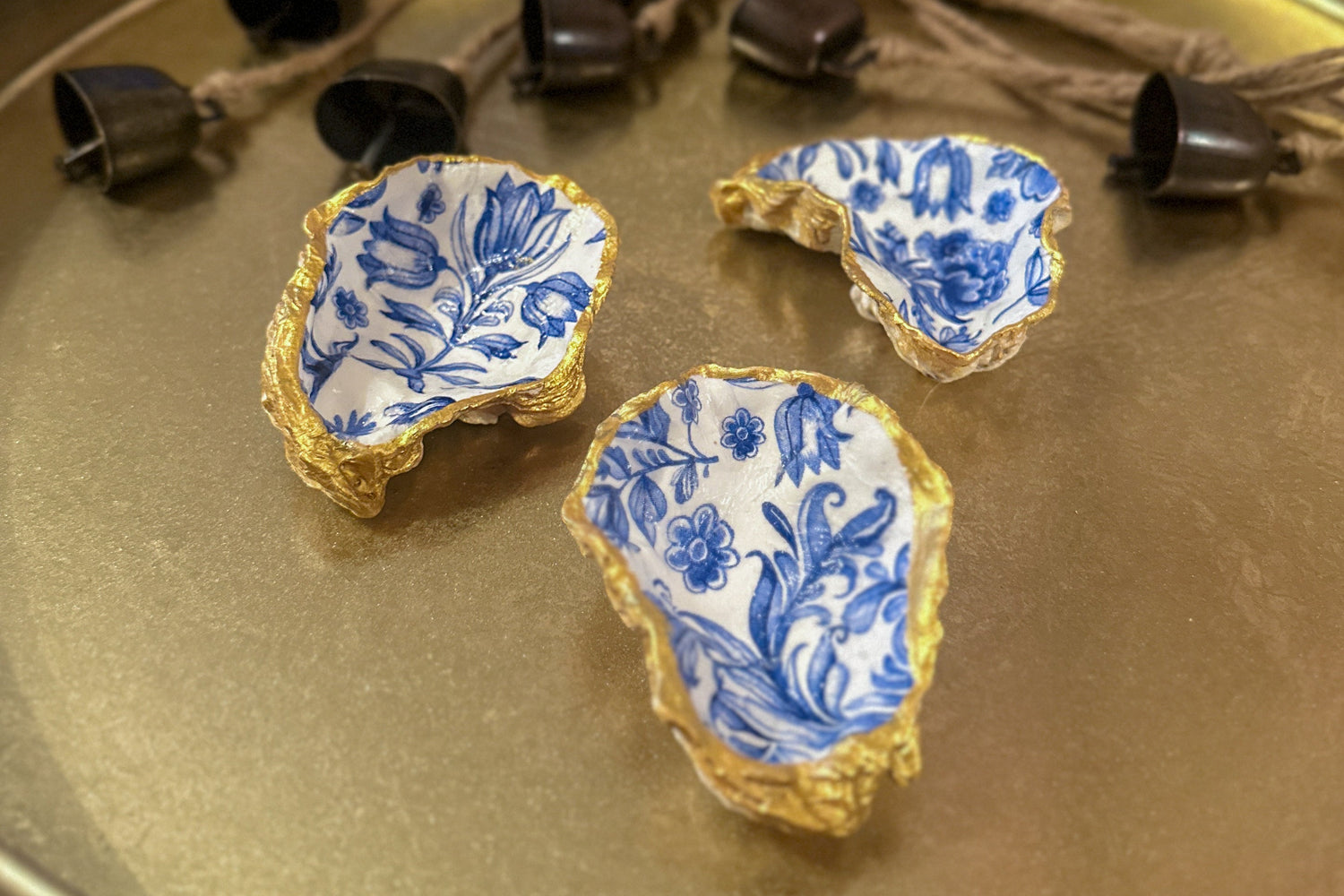 Set of three handmade oyster shell trinket dishes with blue and white floral designs, featuring a decoupage technique and hand-painted gold edges, ideal for home decor or jewellery storage.